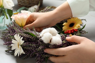 Photo of Florist making beautiful autumnal wreath with heather flowers at light grey table, closeup