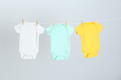 Photo of Different baby onesies hanging on clothes line against light grey background. Laundry day