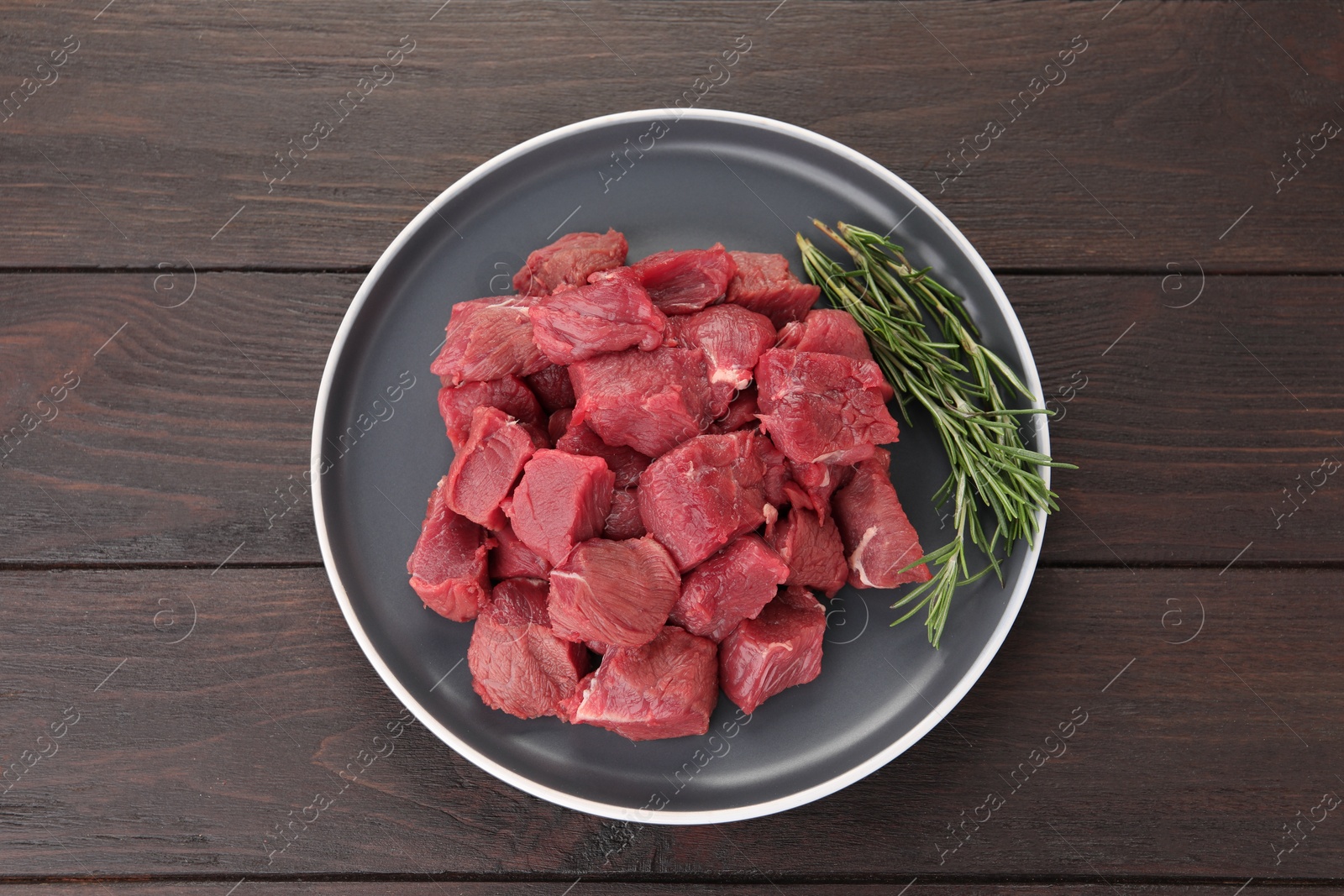 Photo of Pieces of raw beef meat with rosemary on wooden table, top view