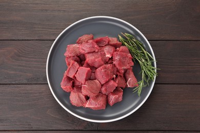 Photo of Pieces of raw beef meat with rosemary on wooden table, top view