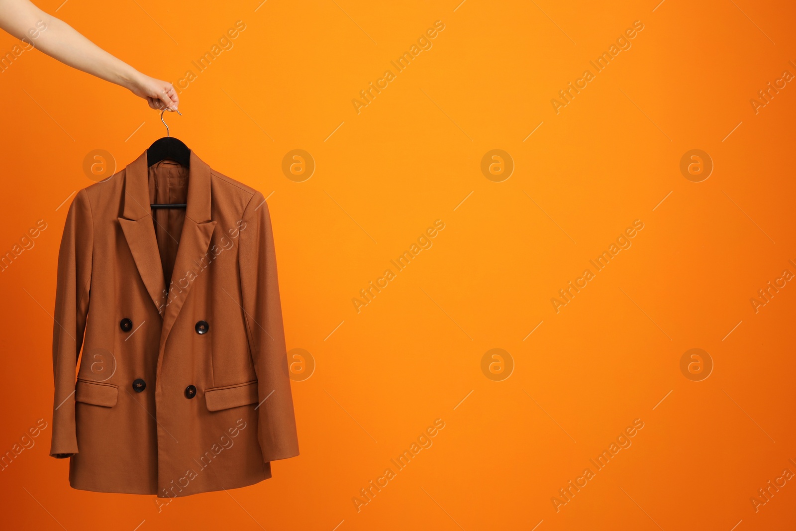 Photo of Woman holding hanger with stylish jacket on orange background, closeup. Space for text