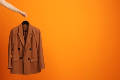 Photo of Woman holding hanger with stylish jacket on orange background, closeup. Space for text
