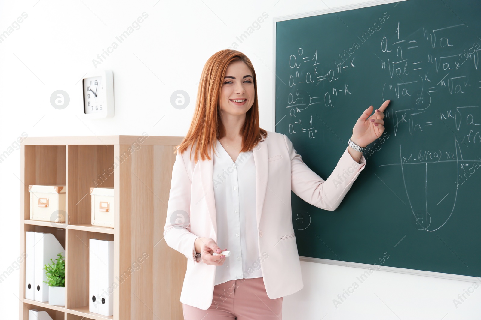 Photo of Beautiful young teacher explaining math formulas written on blackboard in classroom