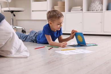 Photo of Cute little boy reading book on warm floor at home. Heating system