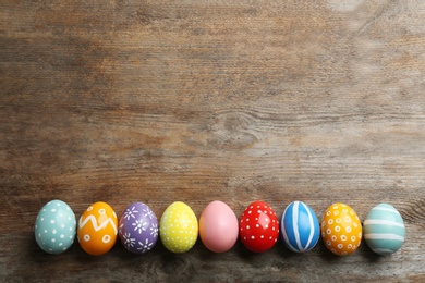 Flat lay composition of painted Easter eggs on wooden table, space for text