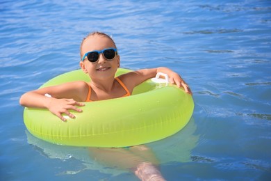 Photo of Happy little girl with sunglasses and inflatable ring in sea on sunny day. Beach holiday