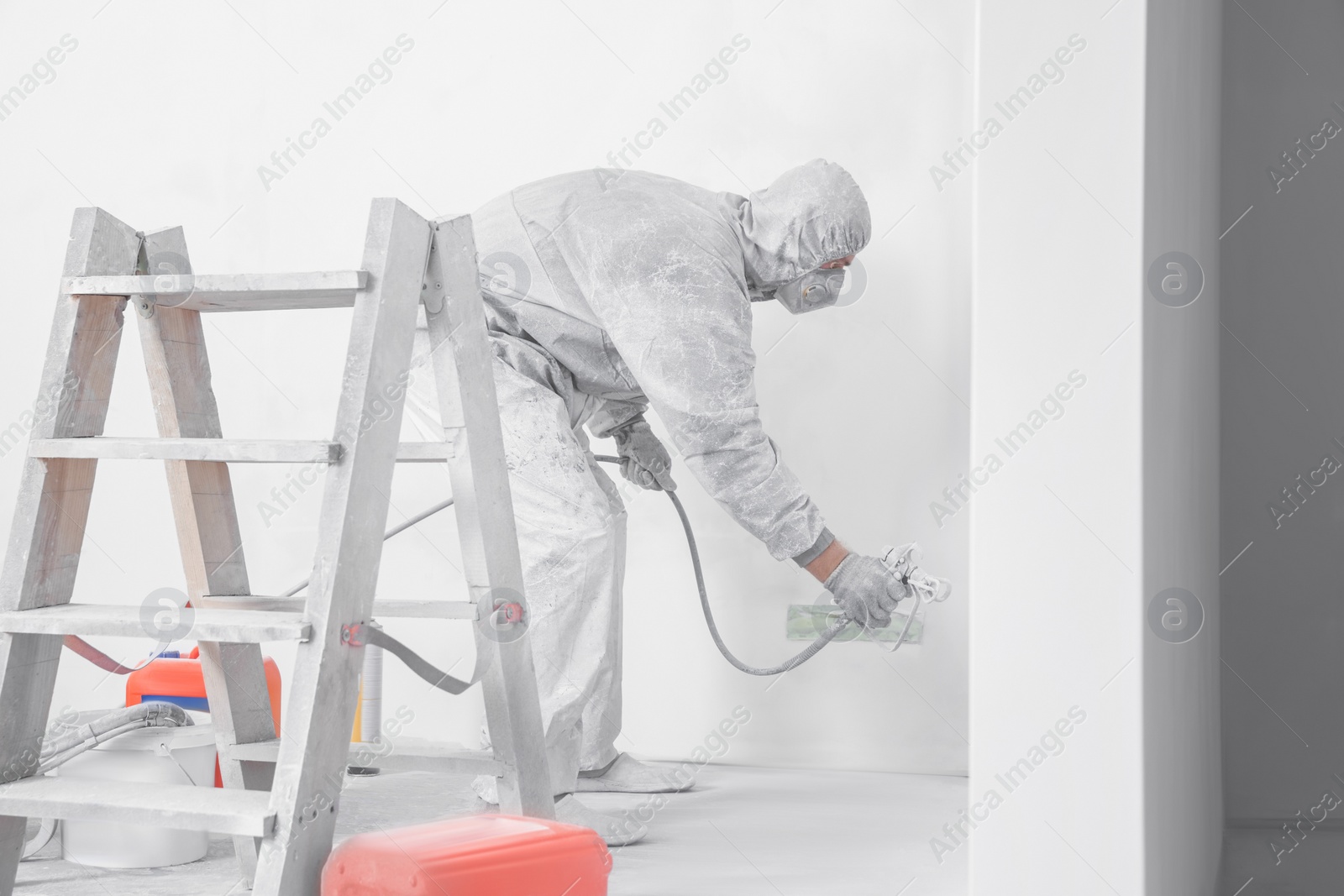 Photo of Decorator in uniform painting wall with sprayer indoors