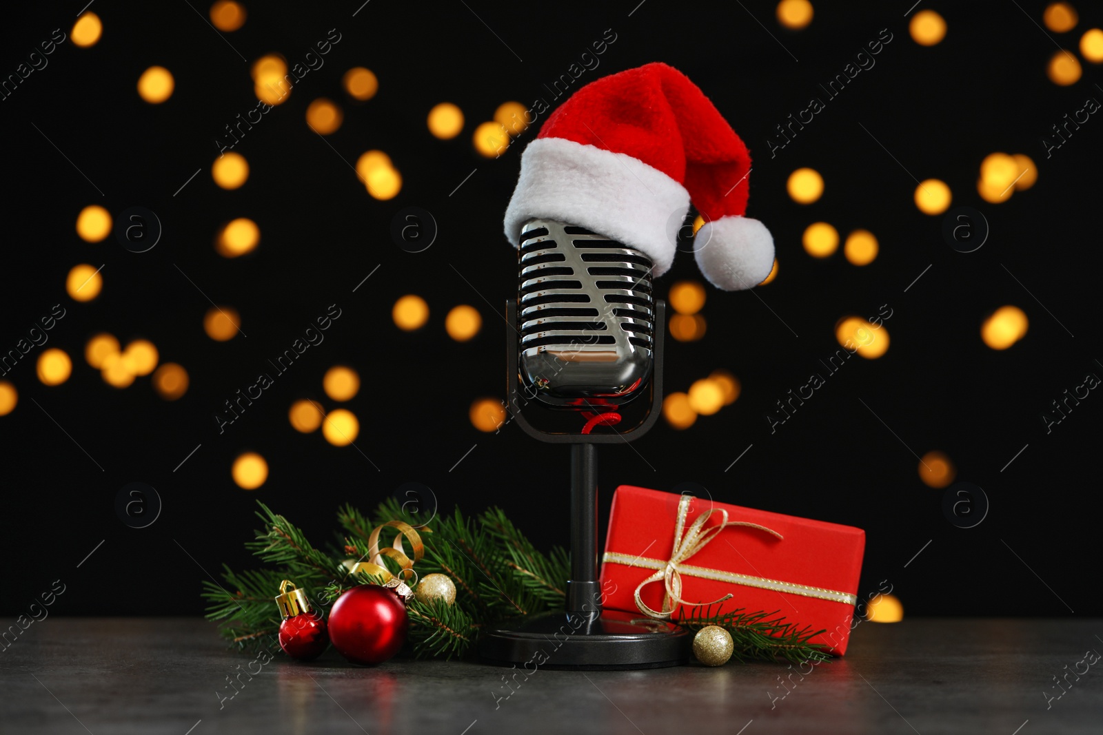 Photo of Microphone with Santa hat and decorations on grey stone table against blurred lights. Christmas music