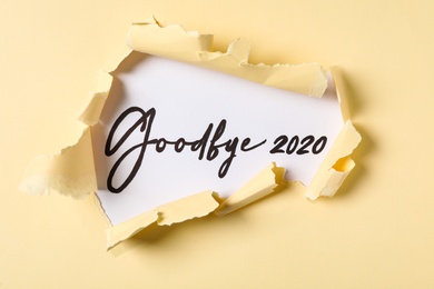 Phrase Goodbye 2020 on white background, view through torn yellow paper