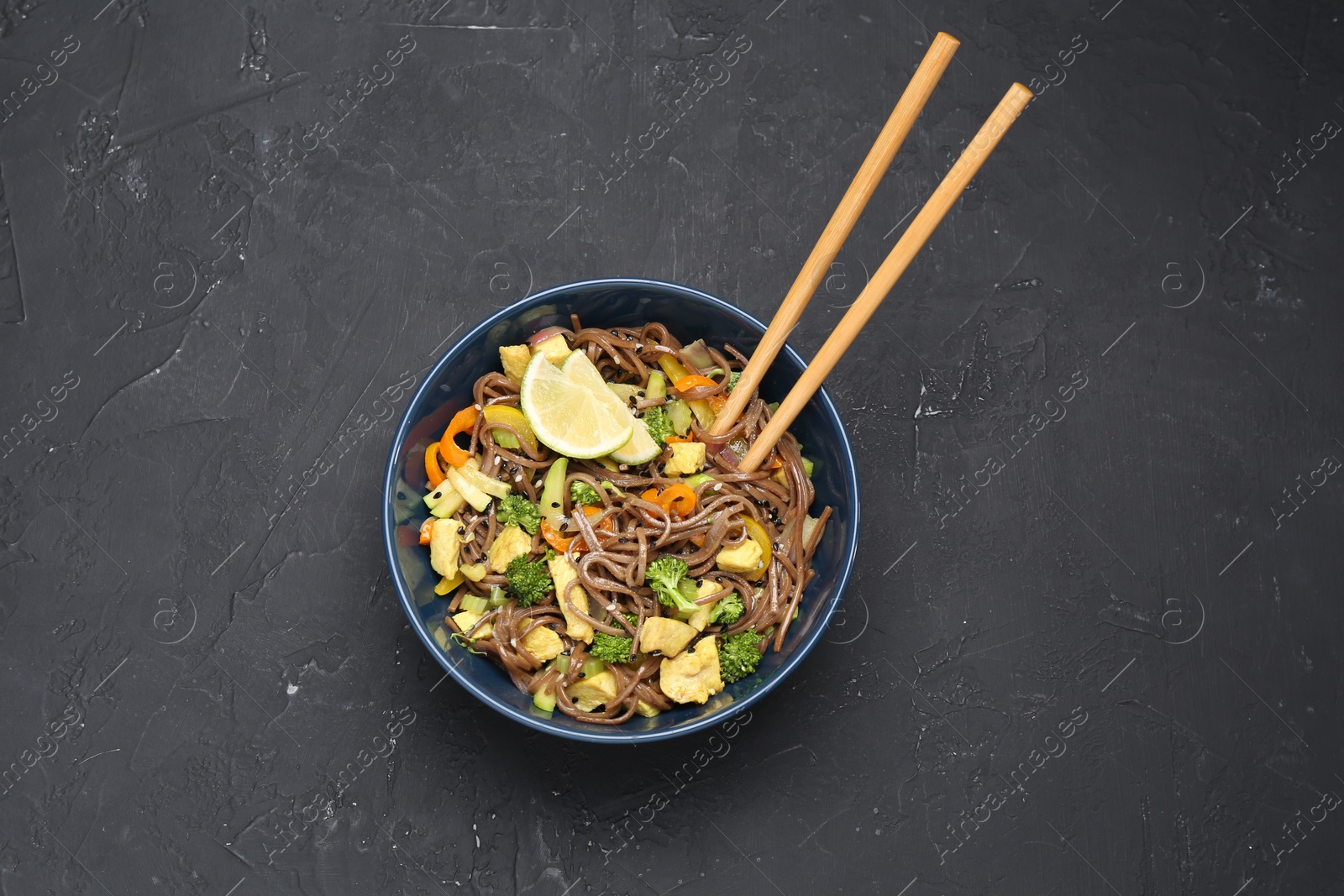 Photo of Stir-fry. Delicious cooked noodles with chicken and vegetables in bowl served on gray textured table, top view