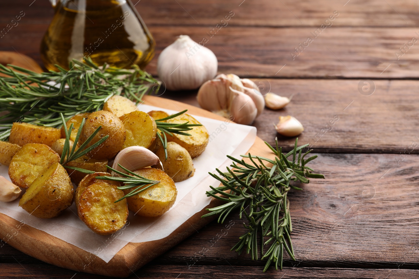 Photo of Delicious baked potatoes with rosemary and garlic on wooden board. Space for text