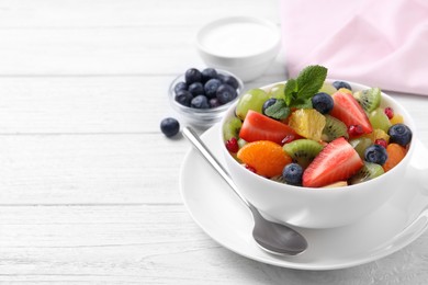 Photo of Delicious fresh fruit salad in bowl on white wooden table, space for text