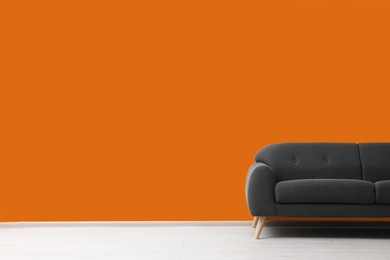 Photo of Stylish grey sofa near orange wall indoors, space for text. Interior design