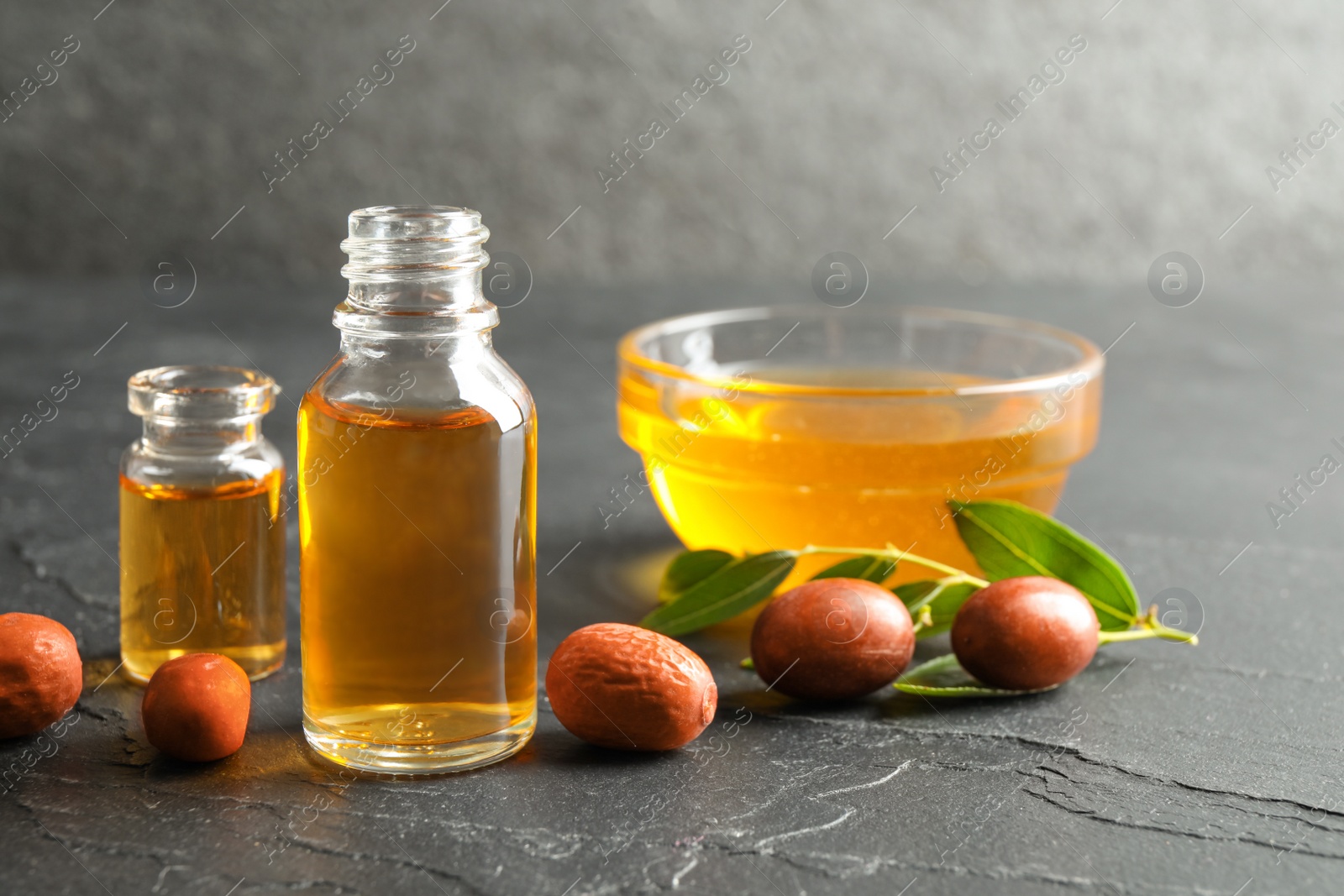 Photo of Jojoba oil and seeds on dark grey table