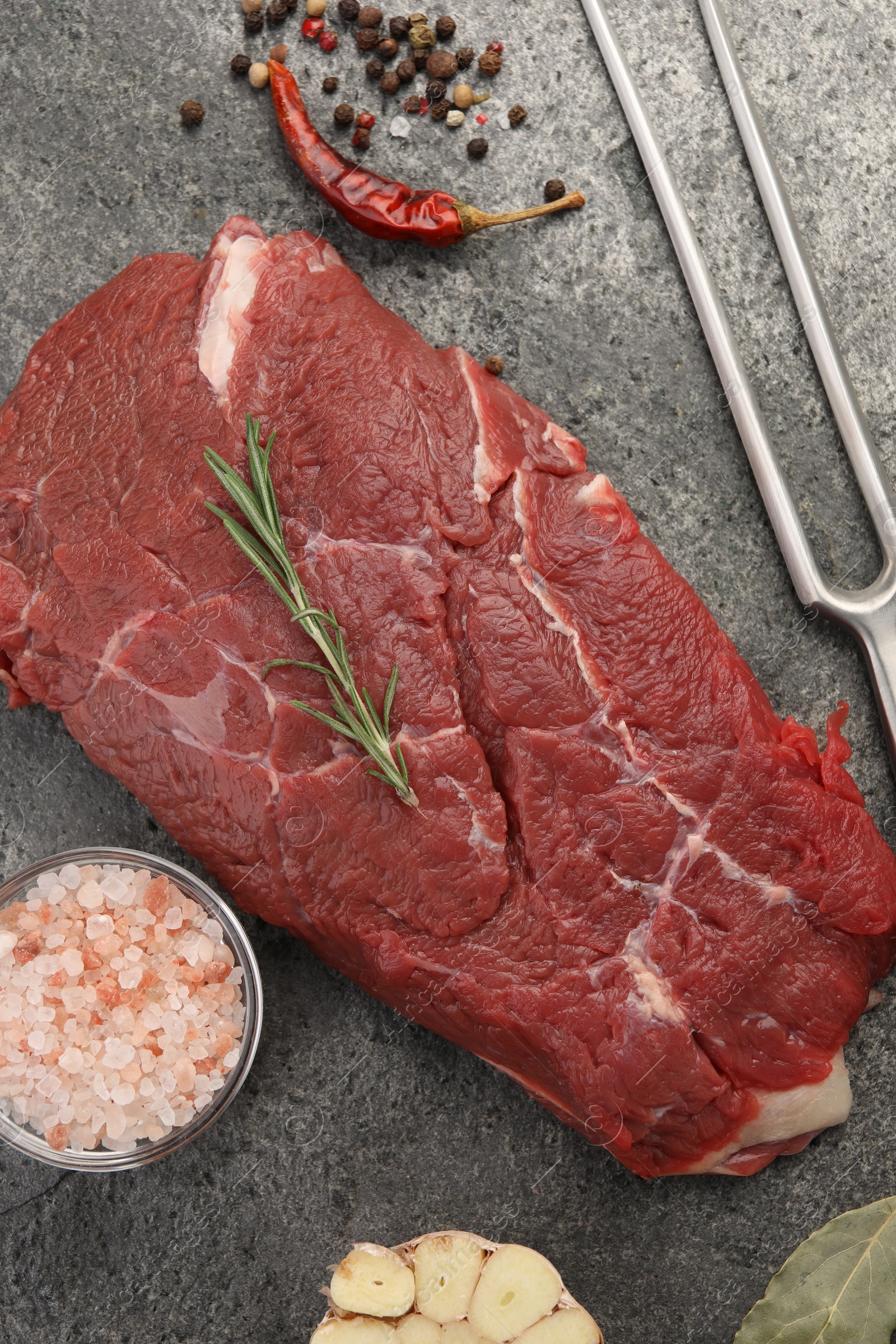 Photo of Piece of raw beef meat, spices, rosemary and fork on grey table, flat lay