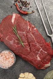 Photo of Piece of raw beef meat, spices, rosemary and fork on grey table, flat lay