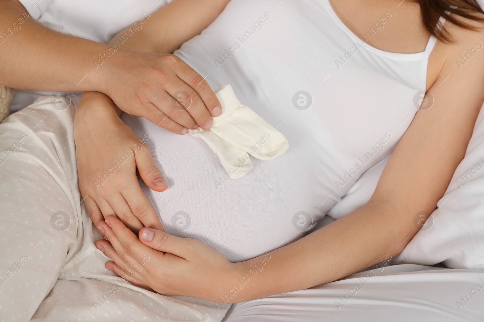 Photo of Man with baby socks hugging his pregnant wife on bed, closeup