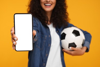 Photo of Happy fan holding soccer ball and showing smartphone on yellow background, closeup