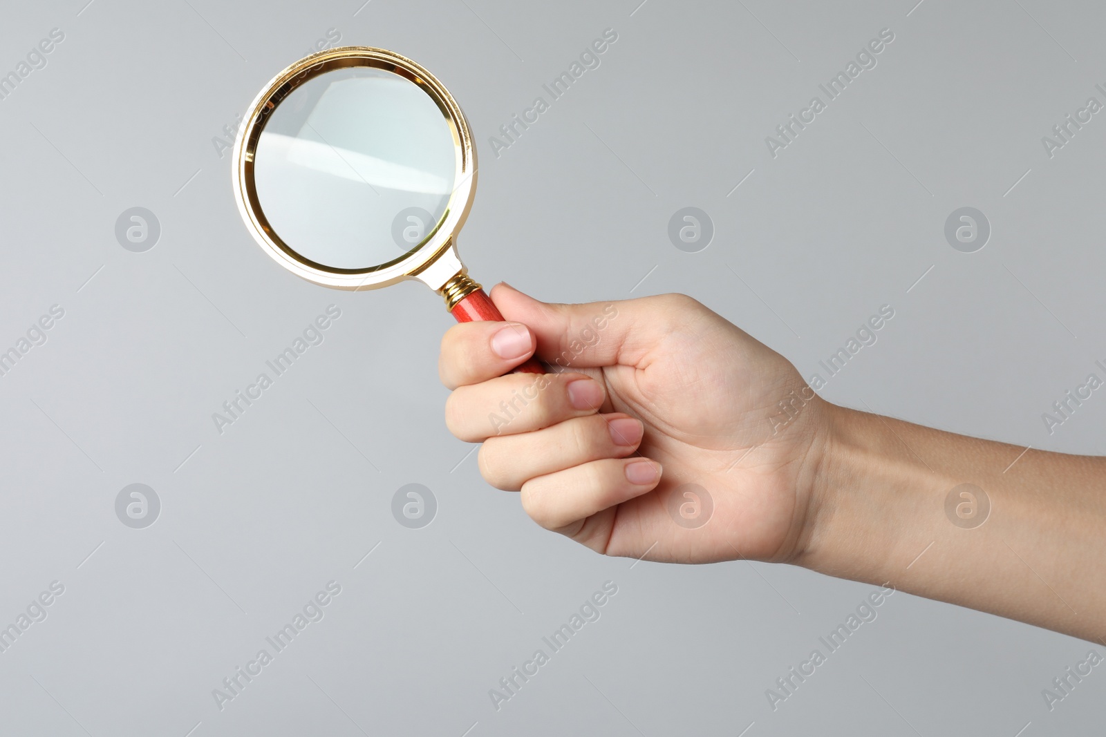 Photo of Woman holding magnifying glass on grey background, closeup. Find keywords concept