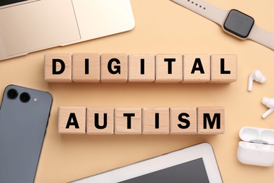 Photo of Phrase Digital Autism made of wooden cubes and devices on beige background, flat lay. Addictive behavior