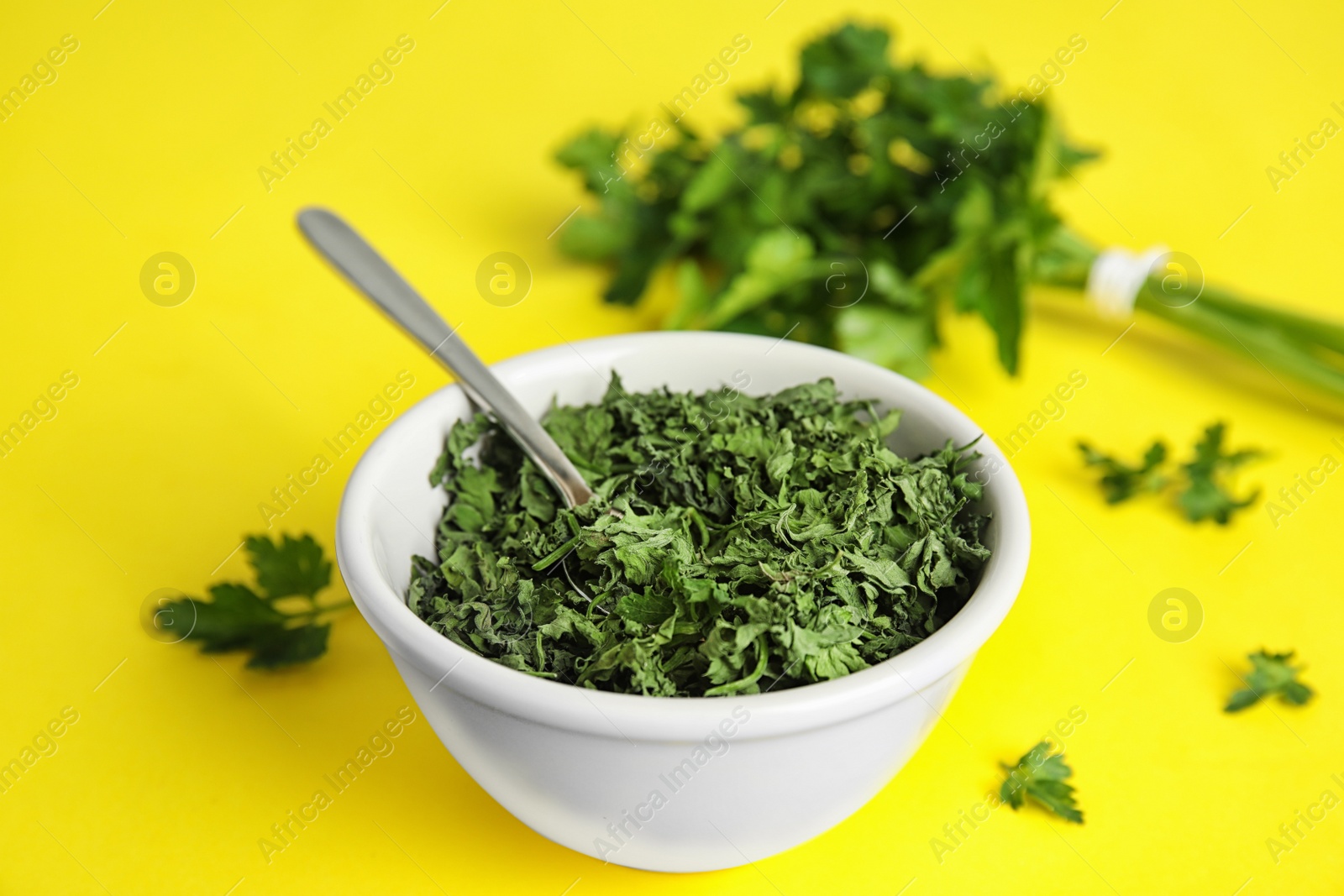 Photo of Bowl with spoon and dried parsley on yellow background