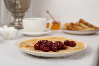 Photo of Pancakes with cherries, vintage samovar and cup of hot drink served on table. Traditional Russian tea ceremony
