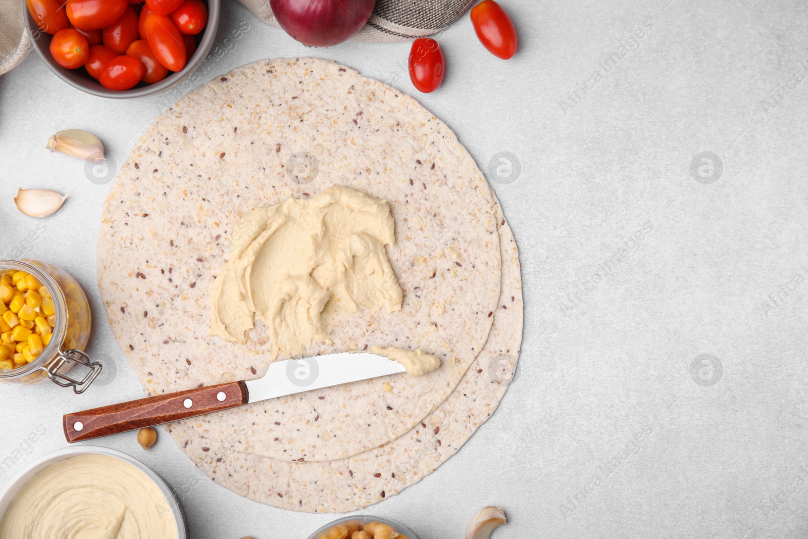 Photo of Tortilla with hummus and vegetables on light table, flat lay. Space for text