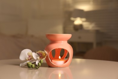 Photo of Aroma lamp with small candle and orchid flower on white table indoors