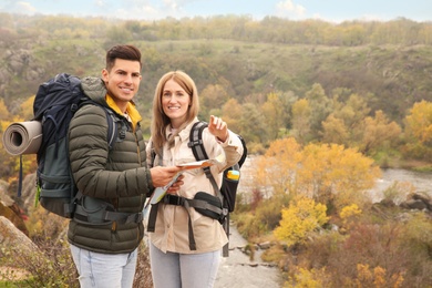 Couple of travelers with backpacks and map enjoying beautiful view near mountain river. Autumn vacation