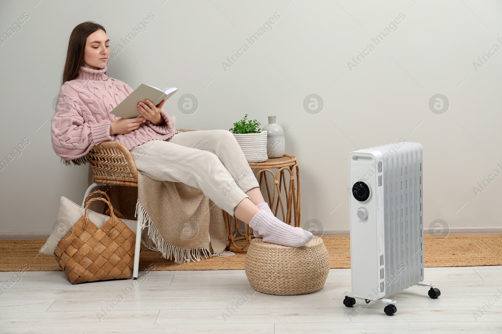 Photo of Woman reading book near modern portable electric heater indoors