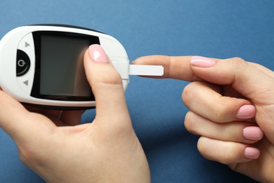 Diabetes. Woman checking blood sugar level with glucometer on blue background, closeup