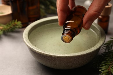 Photo of Woman dripping essential oil into bowl at grey table, closeup. Aromatherapy treatment