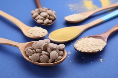 Photo of Spoons with beer yeast powder, flakes and pills on blue background, closeup