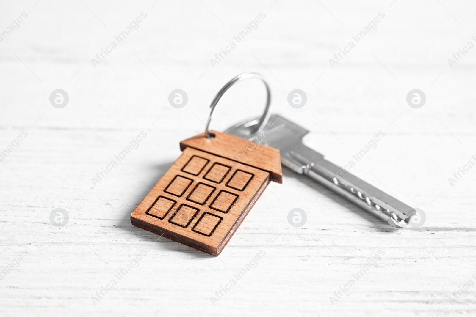 Photo of House key with trinket on white wooden table