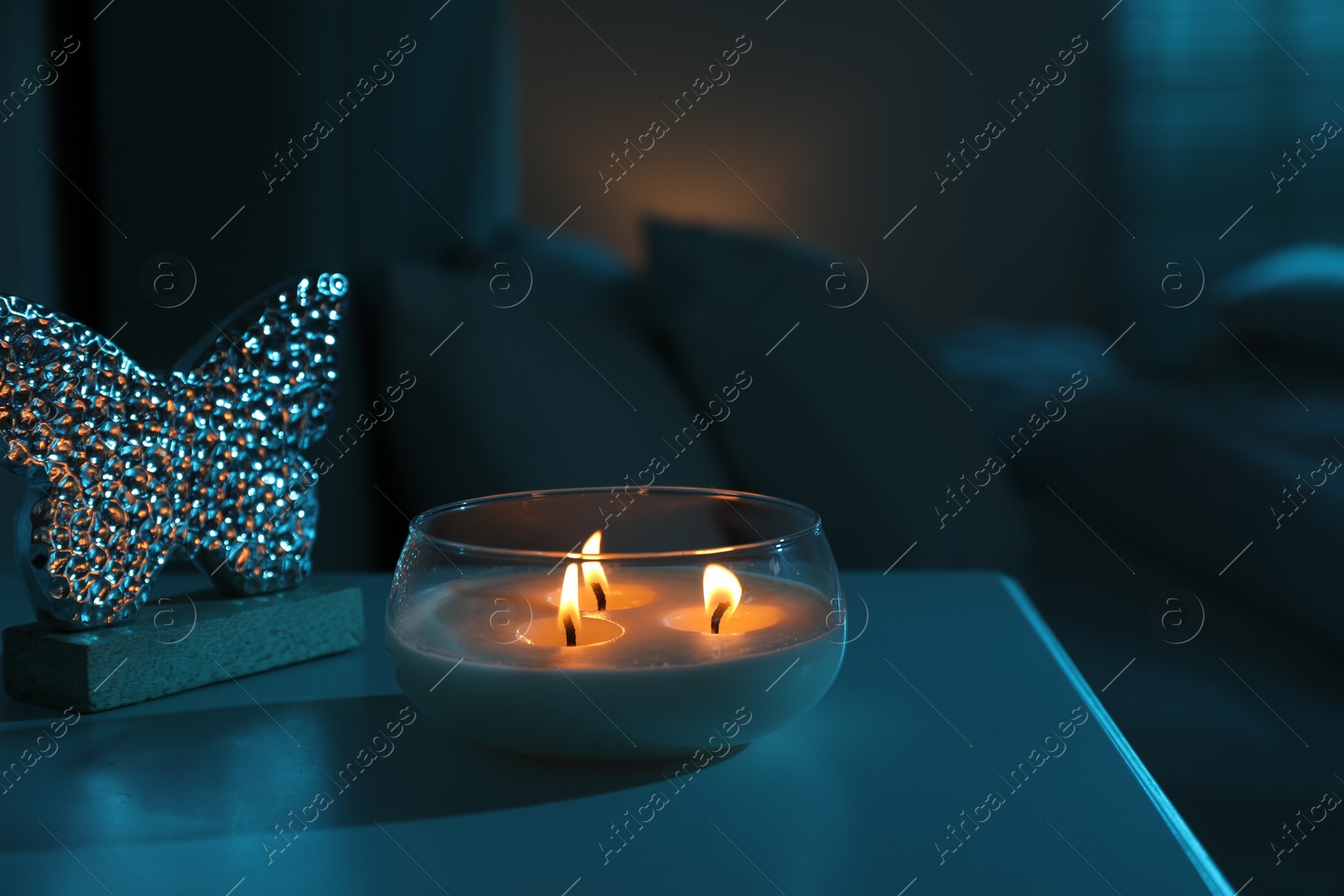 Photo of Burning scented candle on bedside table in bedroom at night