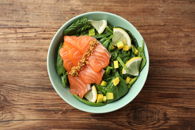 Photo of Delicious salmon with spinach, lemon and avocado in bowl on wooden table, top view