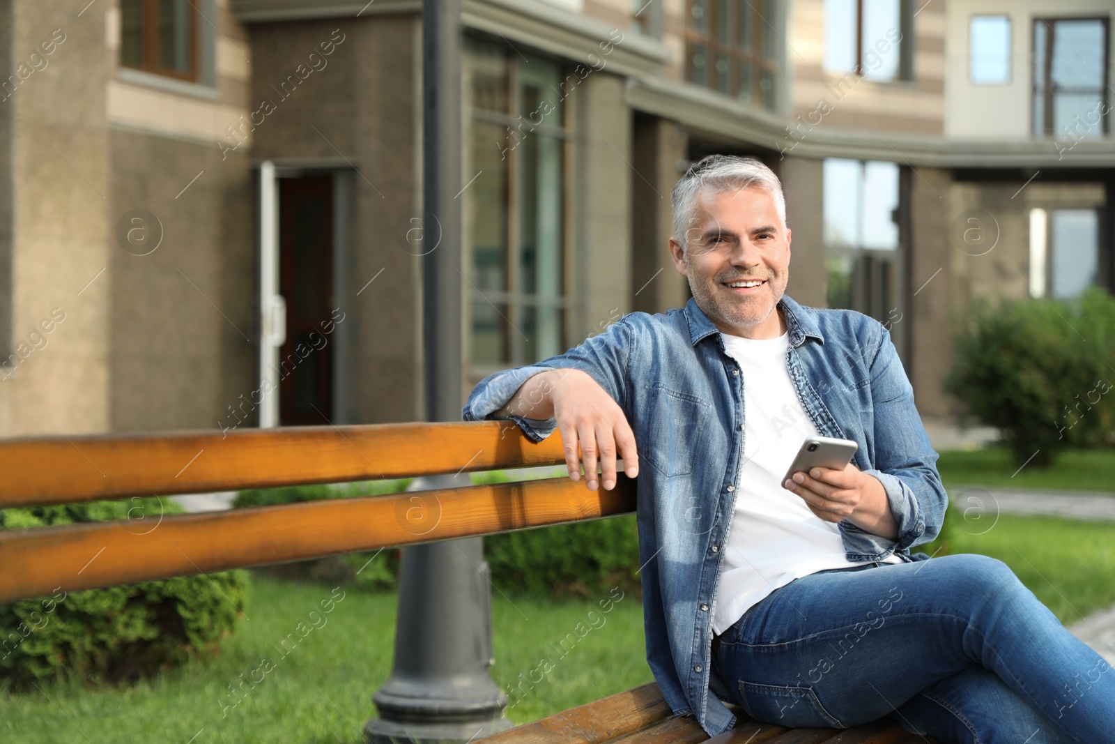 Photo of Portrait of handsome mature man using mobile phone in city. Space for text