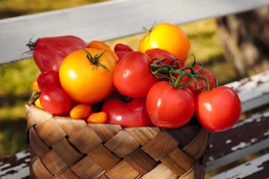 Photo of Basket with fresh tomatoes on old wooden bench outdoors, closeup