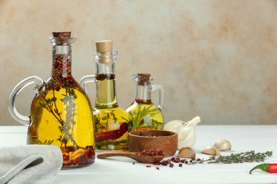 Photo of Cooking oil with different spices and herbs in jugs on white wooden table. Space for text