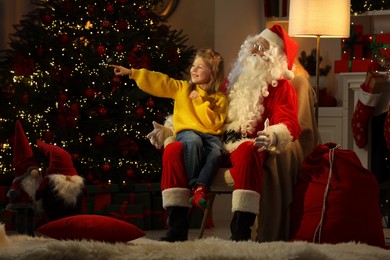Photo of Merry Christmas. Little girl on Santa's knee pointing at something at home