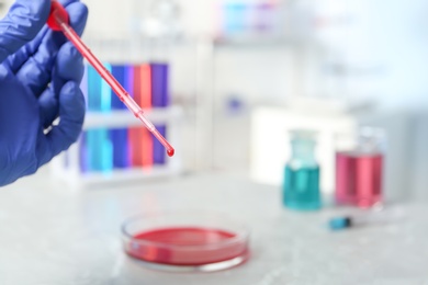 Photo of Scientist dripping reagent into Petri dish with sample in chemistry laboratory, closeup