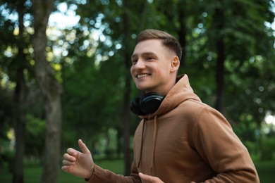 Photo of Smiling man with headphones running in park. Space for text