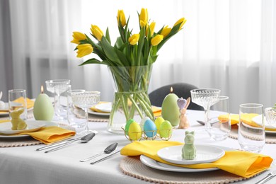 Photo of Festive table setting with glasses, painted eggs and vase of tulips. Easter celebration