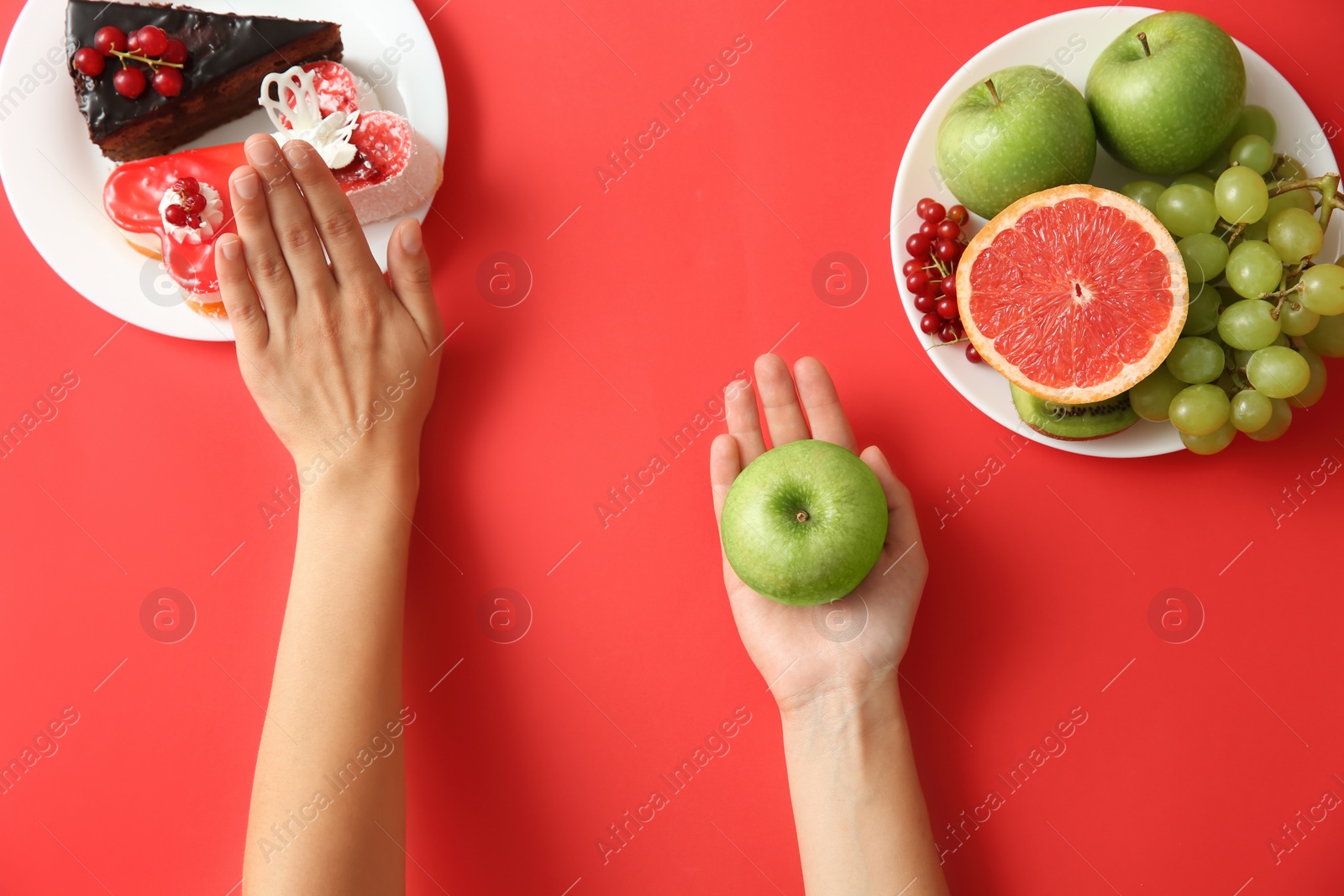 Photo of Top view of woman choosing between sweets and healthy fruits on red background, closeup