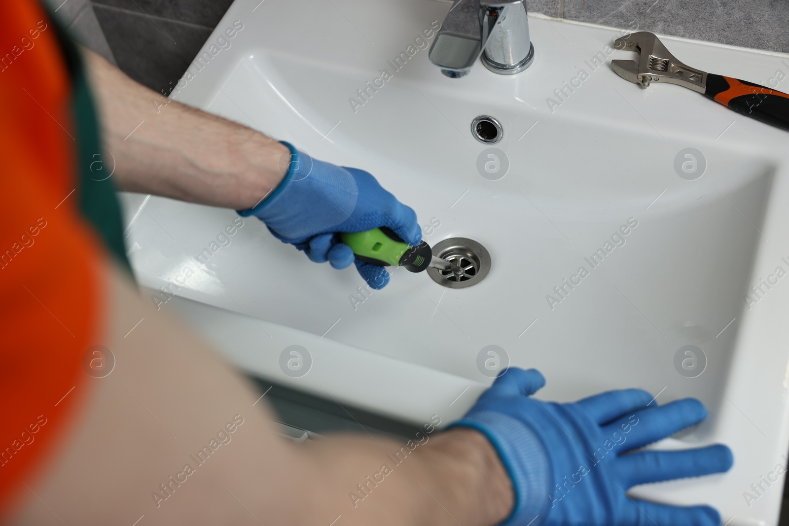 Photo of Plumber in gloves repairing sink with screwdriver, closeup
