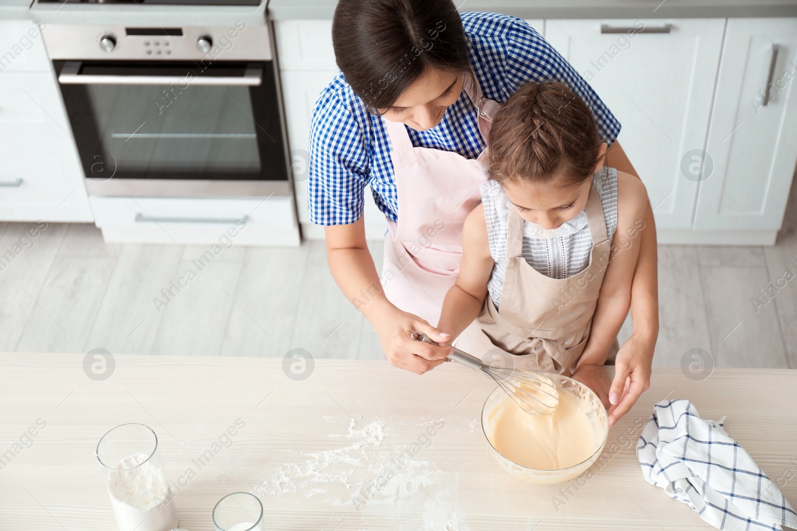 Photo of Mother and her daughter making dough at table in kitchen