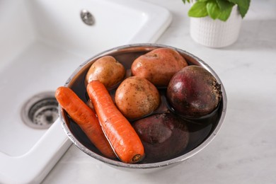 Photo of Fresh vegetables with water in bowl on white countertop. Cooking vinaigrette salad