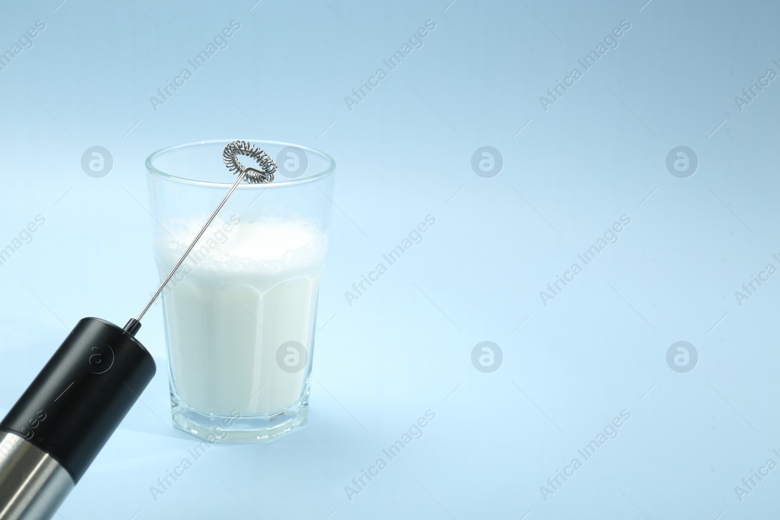 Photo of Mini mixer (milk frother) and whipped milk in glass on light blue background. Space for text