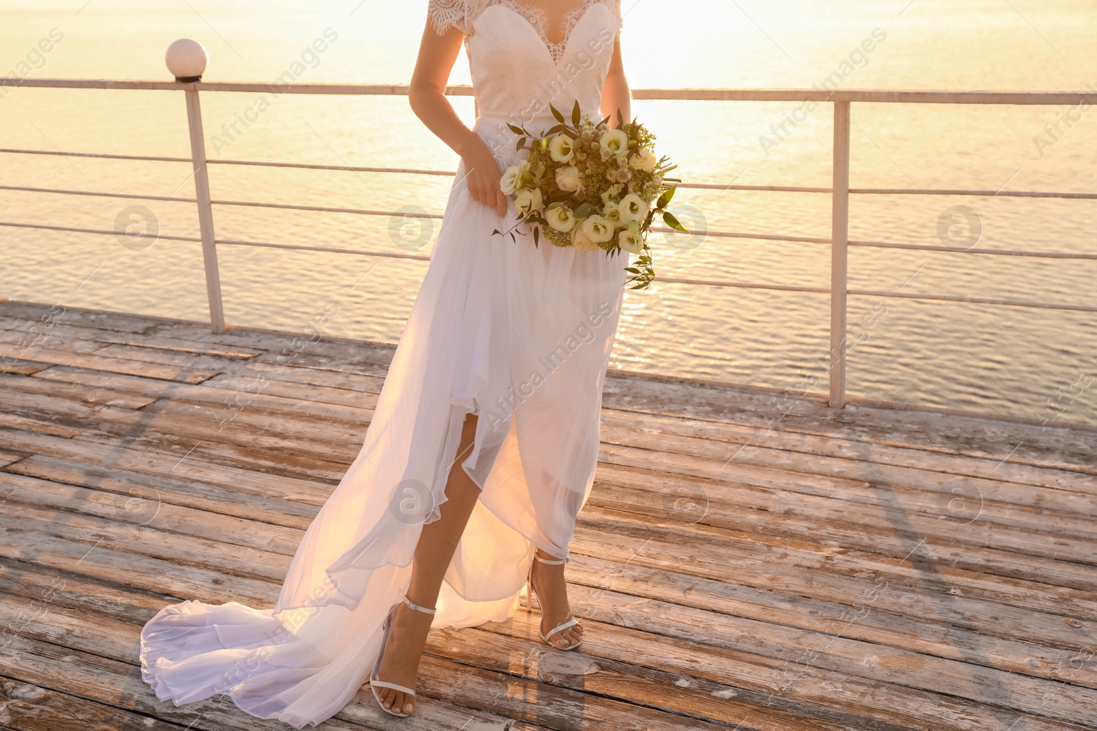 Photo of Bride in beautiful wedding dress with bouquet near river on sunset, closeup