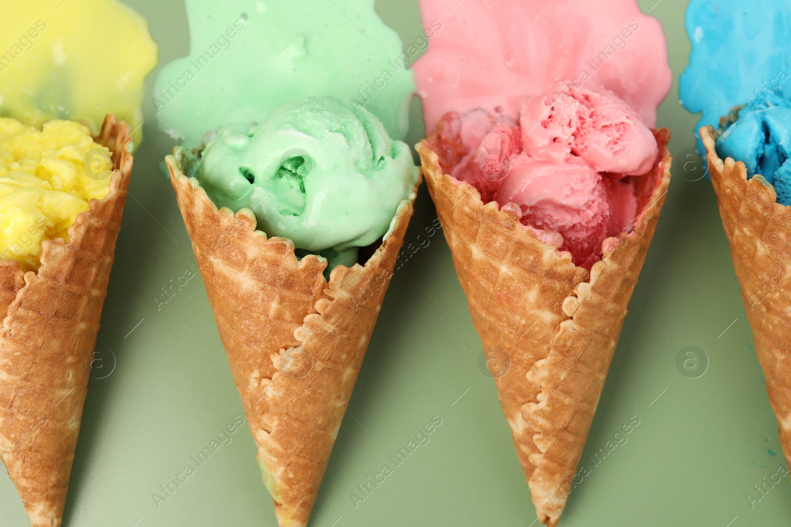 Photo of Melted ice cream in wafer cones on pale green background, flat lay